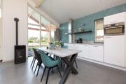 Witte moderne keuken tegen een blauwgrijze wand en een eethoek met 6 kuipstoelen
